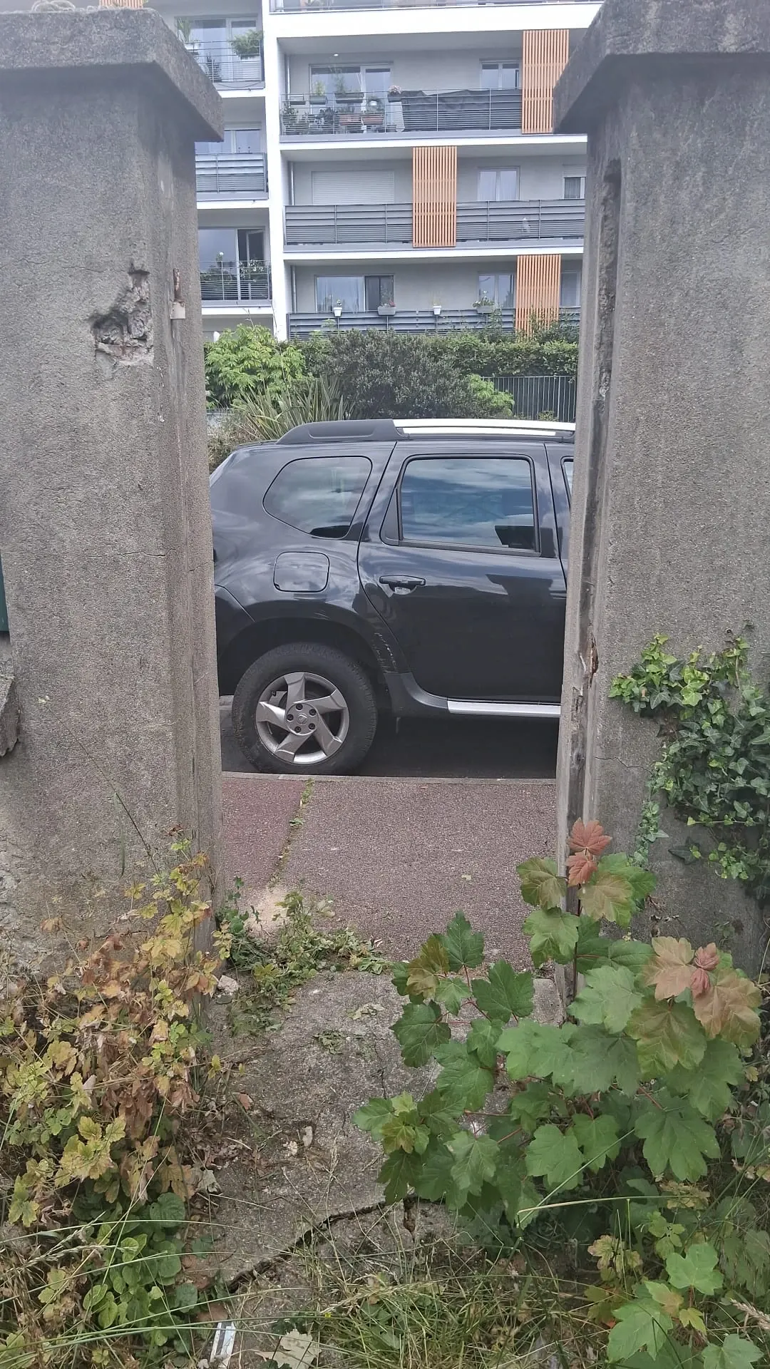 Passage piéton entre deux piliers, devant un véhicule stationné dans la rue
