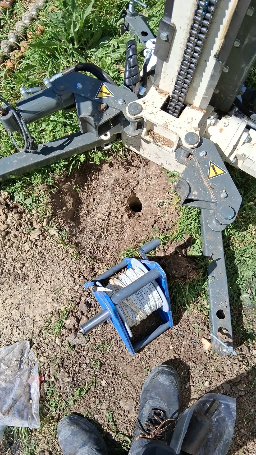 Machine de forage, trou de sondage et ruban de mesure sur un terrain enherbé
